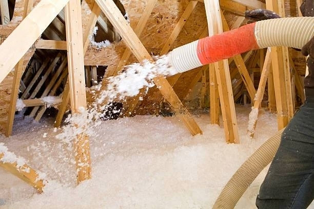 worker-spraying-blown-fiberglass-insulation-between-attic-trusses-transformed